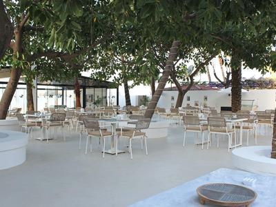 Area pranzo all'aperto con tavoli e sedie bianchi sotto grandi alberi