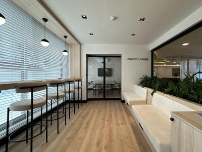 Area d'attesa moderna con sgabelli da bar, pavimento in legno e divani in una stanza luminosa.