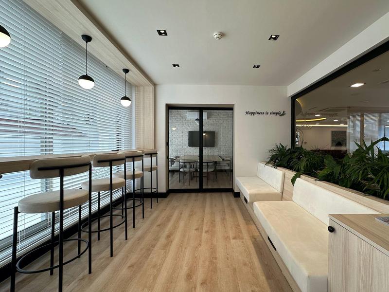 Area d'attesa moderna con sgabelli da bar, pavimento in legno e divani in una stanza luminosa.