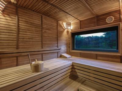 Hohe Holzwände und -bänke bilden eine helle, rustikale Sauna mit großem Fenster und Holz-Eimer mit Kelle.