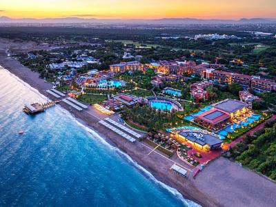Küste mit Strand, blauem Meer, Hotels und beleuchteten Pools bei Sonnenuntergang.