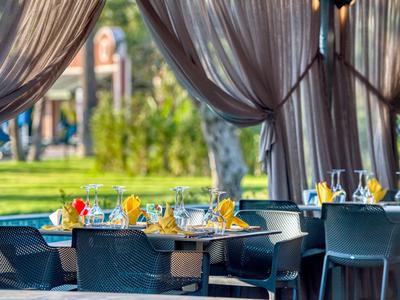 Freiluftrestaurant mit gedeckten Tischen, bunten Servietten und grauen Stühlen unter Vorhängen.