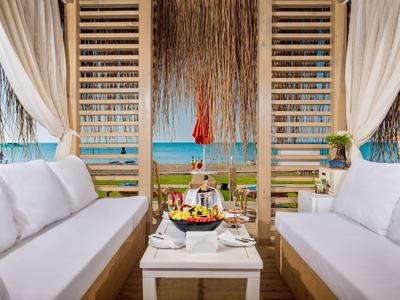 Luxuriöser Strandpavillon mit weißen Sofas, Holztisch und tropischer Fruchtplatte am Meer.