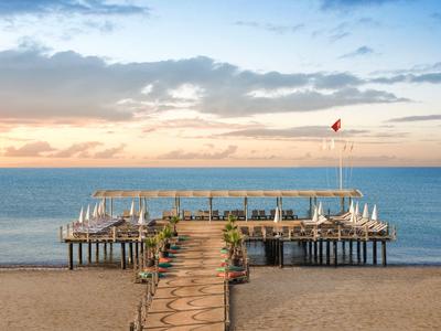 Steg mit Sitzplätzen am Strand, ins ruhige Meer hinausragend, bei Sonnenuntergang mit wolkigem Himmel.