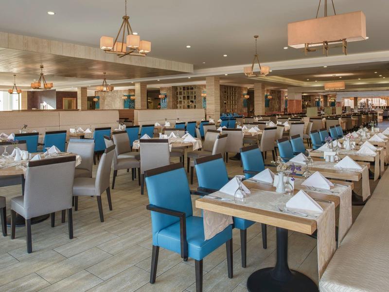 Spacious hotel restaurant with modern blue and gray chairs and neatly set tables.