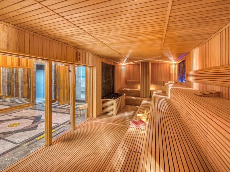 Spacious wooden sauna with large glass doors and tiered seating inside.