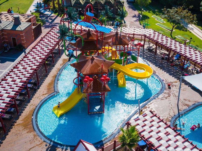 A colorful water park with slides and pools surrounded by red and white buildings in a sunny area.