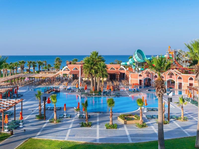 Large outdoor water park with pools, waterslides, and palm trees under a clear blue sky.