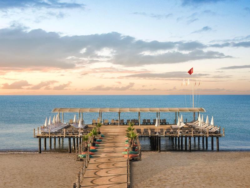 Wooden pier extending into calm sea with lounge chairs and umbrellas at sunset.