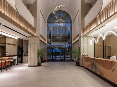 Hotel lobby with high ceilings, bar on the left, reception desk on the right under warm modern lighting.
