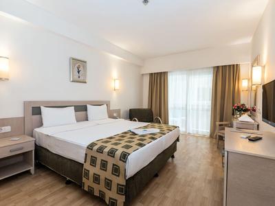 Bright hotel room with double bed, nightstands, and balcony with curtains.