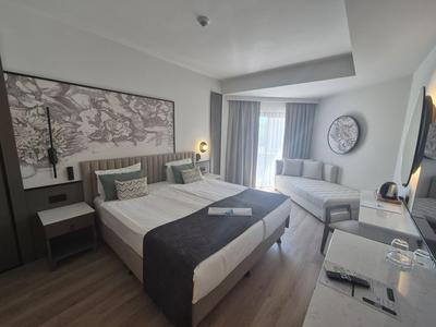 Nowoczesny pokój hotelowy z łóżkiem podwójnym, sofą i dużym oknem z zasłonami.