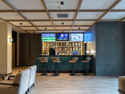 Nowoczesny bar hotelowy z drewnianym sufitem, ladą, stołkami barowymi i oświetlonymi półkami z napojami.