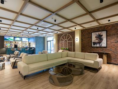 Nowoczesny hotelowy salon z beżową narożną sofą, szklanymi stolikami i ceglanym murem z dziełem sztuki.