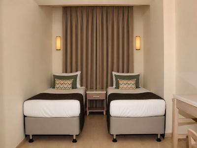 Hotelzimmer mit zwei Einzelbetten, einem Nachttisch und gedämpfter Beleuchtung.