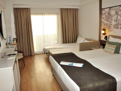 Modern eingerichtetes Hotelzimmer mit Betten, Fernseher und Vorhängen am Fenster.