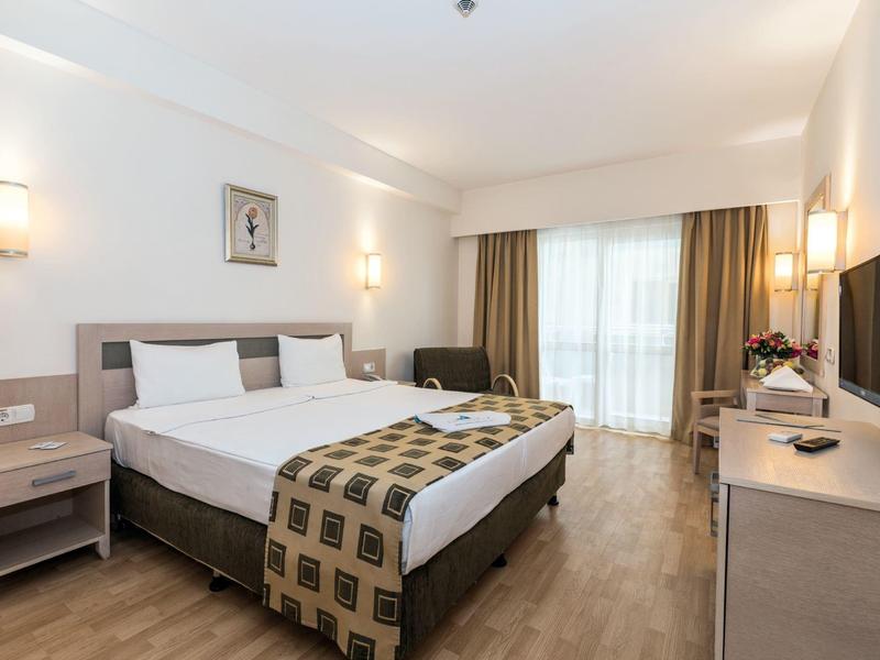Bright hotel room with double bed, nightstands, and balcony with curtains.