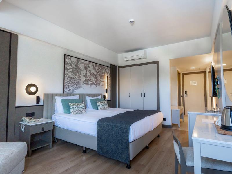 Modern hotel room with large bed, wardrobe, desk, and stylish lighting.