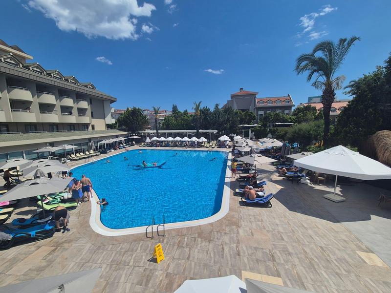 Large hotel pool with sun loungers and umbrellas under a clear sky.