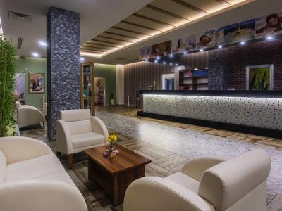 Moderne Hotelrezeption mit dunklem Tresen, weißen Sesseln und warmem, indirektem Licht.