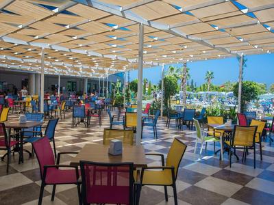 Große Terrasse mit bunten Stühlen und Tischen unter einem hellen Sonnendach bei klarem Himmel.