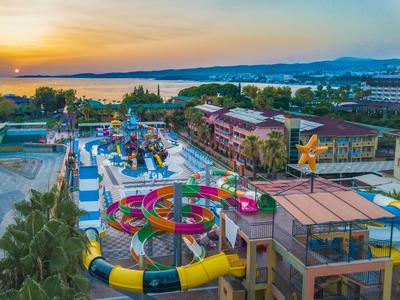 Bunter Wasserpark mit Rutschen, Pools und Gebäuden am Meer bei Sonnenuntergang.