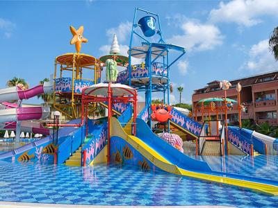 Bunter Wasserspielplatz mit Rutschen und Planschbecken vor Hotelgebäude an sonnigem Tag