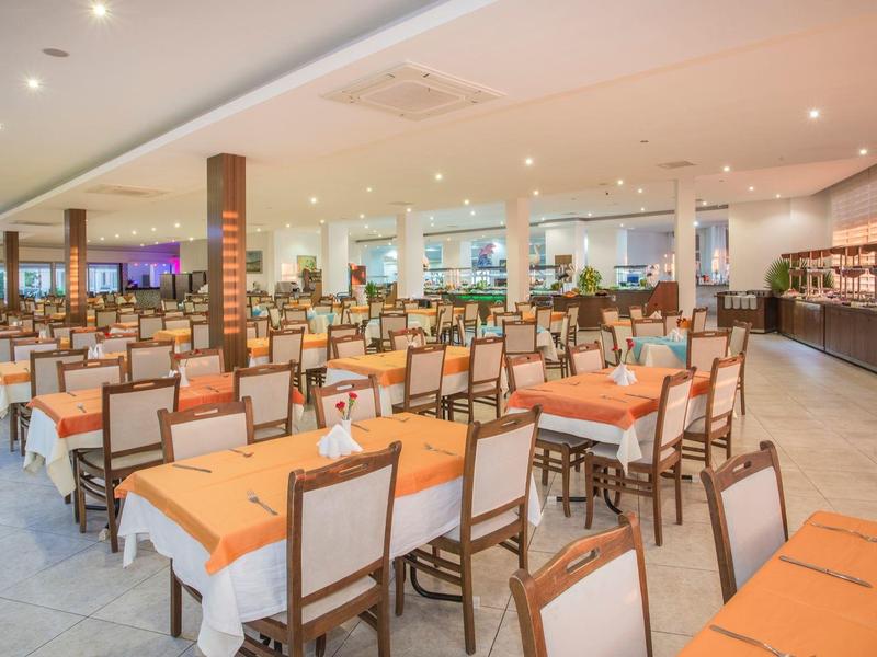 Großer moderner Speisesaal mit zahlreichen Tischen und Stühlen, die mit orangen Tischdecken dekoriert sind.