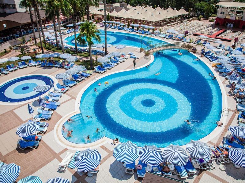 Großer Hotelpool mit blauen Kreisen, Sonnenliegen und Sonnenschirmen im Außenbereich.