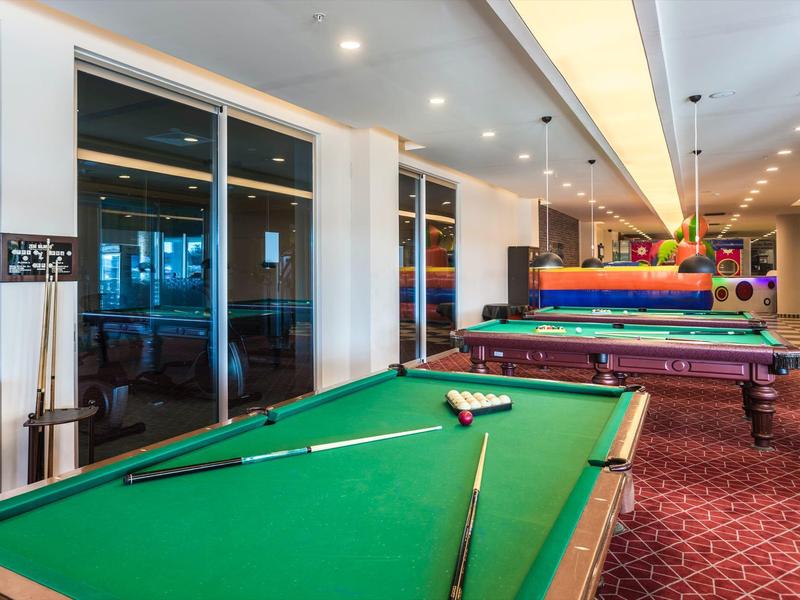 Spielzimmer mit mehreren Billardtischen in einem Hotel mit Teppichboden und moderner Beleuchtung.