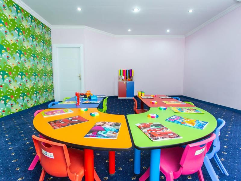 Bunter Kinderspielraum mit bunten Tischen, Stühlen und Spielzeugen vor grüner Wand.