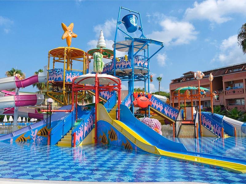 Bunter Wasserspielplatz mit Rutschen und Planschbecken vor Hotelgebäude an sonnigem Tag