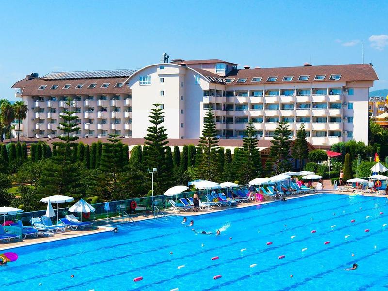 Großes Hotel mit mehreren Stockwerken neben einem großen Außenpool mit Sonnenschirmen.