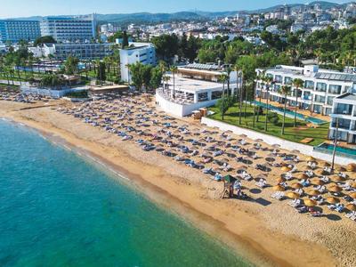 Vista de una larga playa de arena con tumbonas frente a un hotel costero y agua clara del mar.
