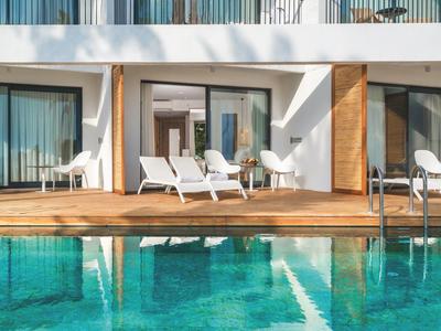 Área de piscina moderna con terraza de madera y tumbonas blancas frente a ventanas del hotel.