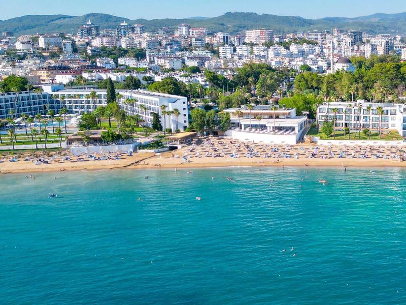 Ciudad costera con playa de arena, hoteles y mar azul claro bajo cielo nublado.