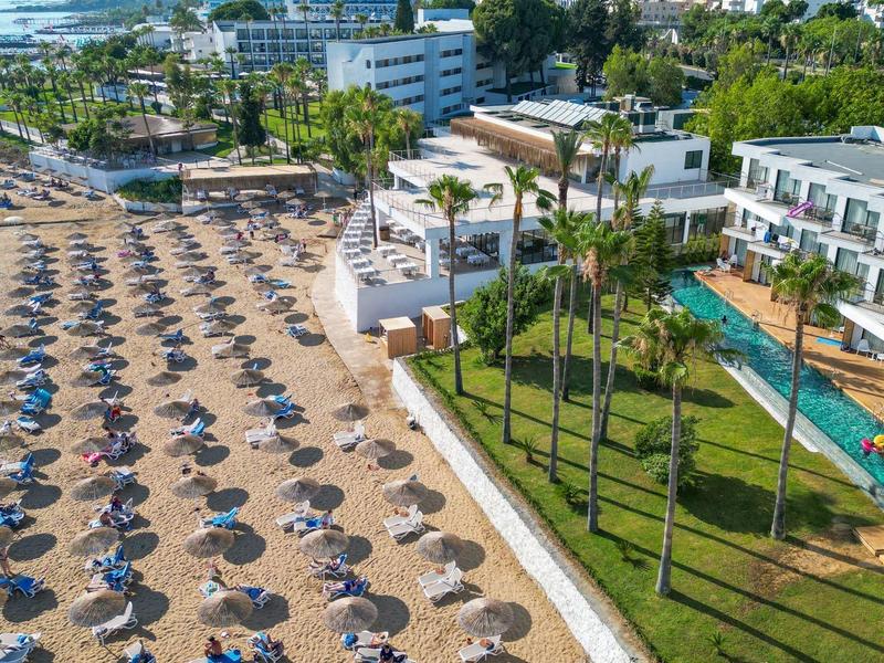 Complejo hotelero con tumbonas en la playa, zona de piscina y palmeras en un día soleado.