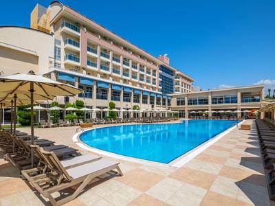 Hôtel moderne avec grande piscine et de nombreuses chaises longues sous parasols par ciel dégagé.