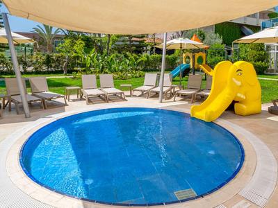 Piscine ronde pour enfants avec toboggan jaune et chaises longues dans le jardin de l'hôtel.