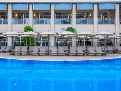 Piscine bleue d'hôtel avec chaises longues et parasols blancs, bâtiment moderne en arrière-plan.
