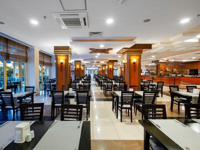 Intérieur spacieux de restaurant d'hôtel avec de nombreuses tables, chaises et grandes fenêtres.