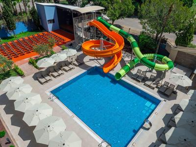 Piscine d'hôtel avec deux toboggans colorés, chaises longues et parasols dans un cadre verdoyant.