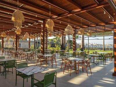 Terrasse d'hôtel ouverte et couverte avec de nombreuses tables et chaises, vue sur la verdure et les palmiers.