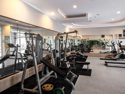 Salle de sport moderne avec équipements de musculation et cardio, grands miroirs et éclairage lumineux.