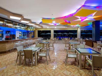 Bar d'hôtel moderne avec tables et chaises en verre, éclairage coloré au plafond, vue ouverte de nuit.