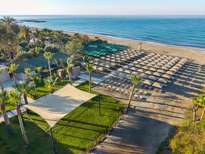 Plage avec parasols et voiles d'ombrage près d'un hôtel et de palmiers.