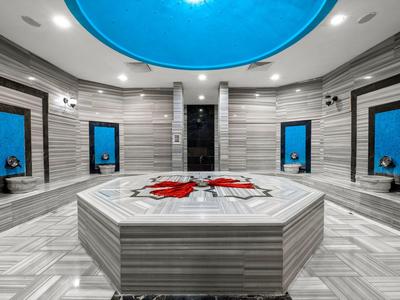 Hammam turc moderne avec murs en marbre, bassin central et fenêtre de plafond éclairée en bleu.