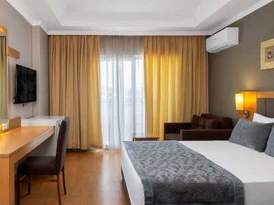 Chambre d'hôtel moderne avec lit double, bureau, télévision et accès au balcon avec rideaux.