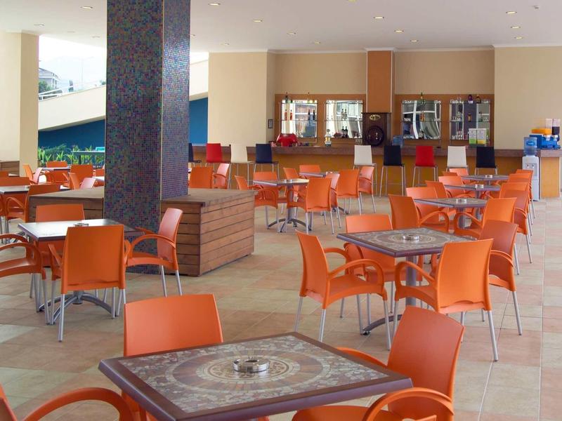 Großer, heller Speisesaal mit orangefarbenen Stühlen und quadratischen Tischen mit Muster.