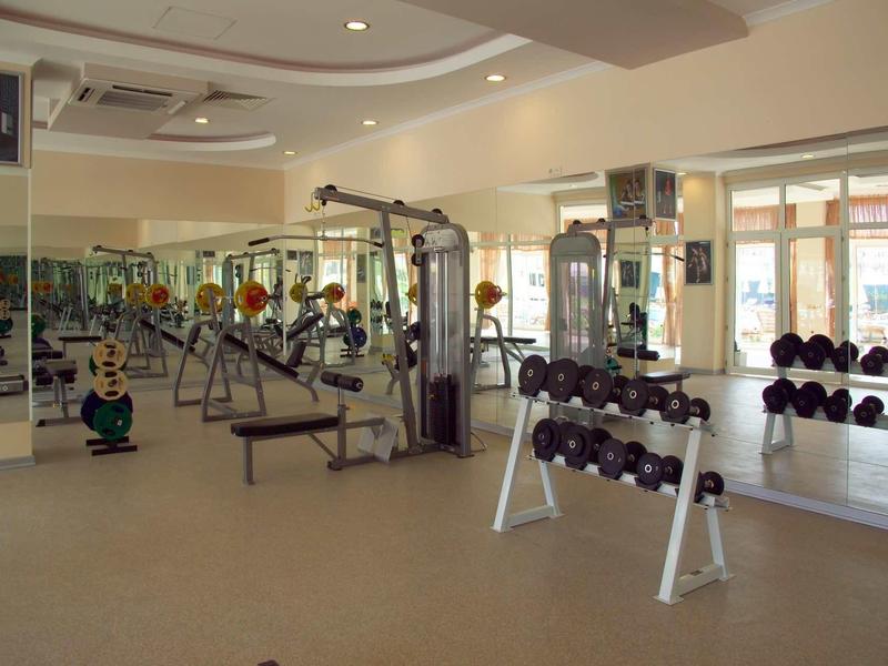 Großer heller Fitnessraum mit Hanteln, Kraftmaschinen und großen Spiegelwänden an der Wand.